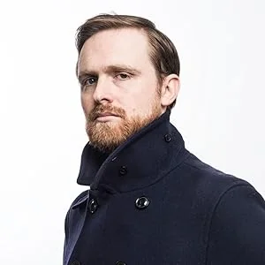 Adam Biles in navy coat showcasing personal style.