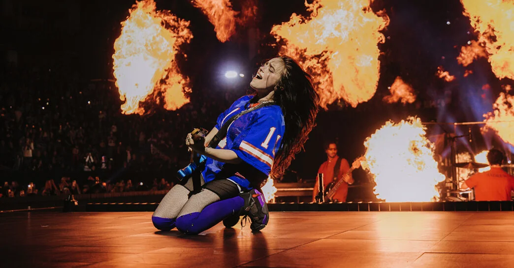 Billie Eilish performing live with flames, hinting at new album after tour finale.