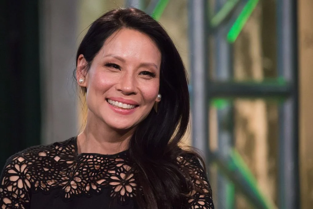 Lucy Liu smiling in a black outfit during an event.