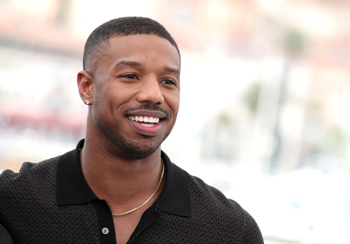 Michael B. Jordan smiling at a press event, showcasing his charm.