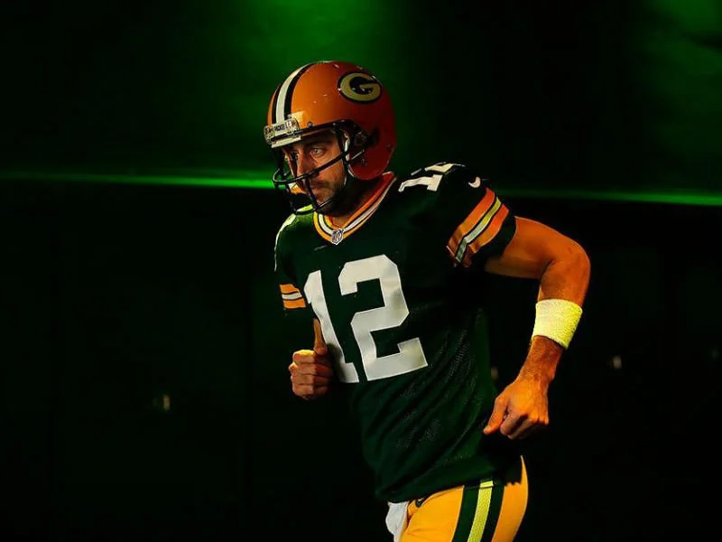 Aaron Rodgers running onto the field, showcasing his religion and athletic spirit.