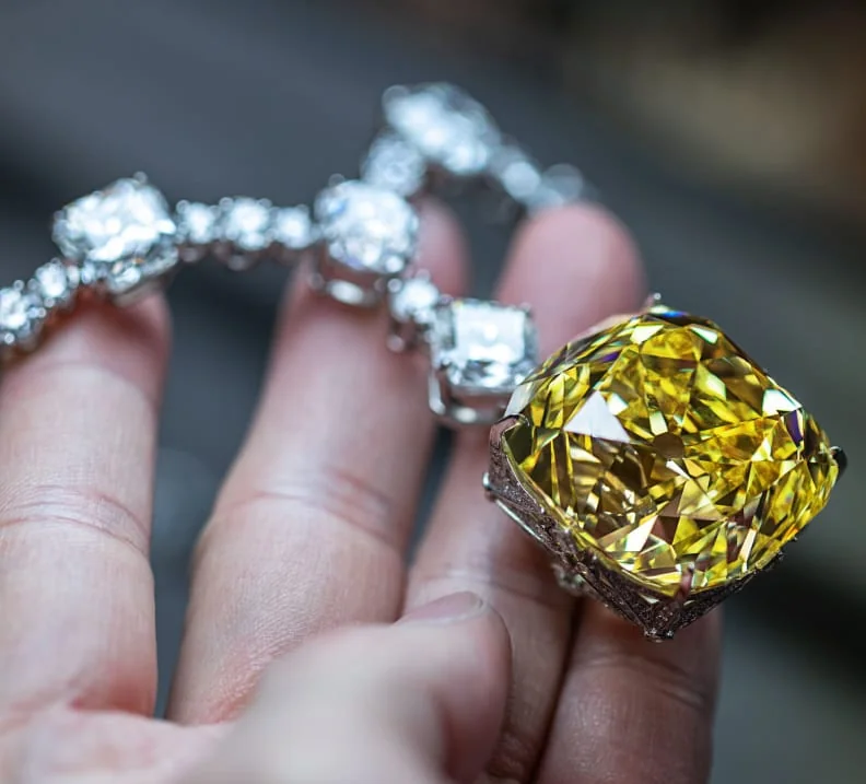 Close-up of a hand holding a yellow diamond necklace like the Lady Gaga ring.